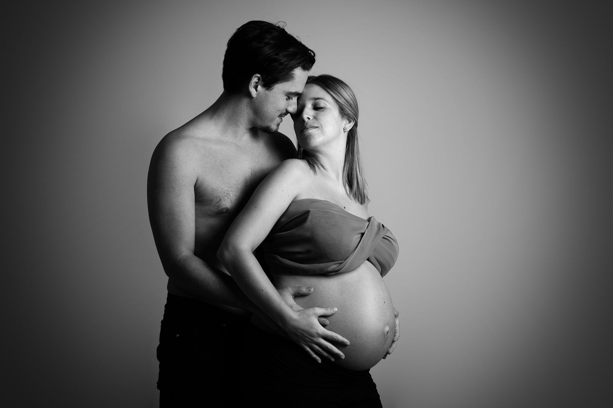 Couple tendre lors d’une séance photo grossesse en studio, la future maman mettant en valeur son ventre arrondi